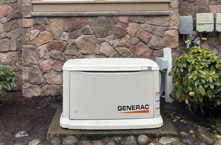 A Generac home generator on a concrete pad next to a stone wall and bushes.