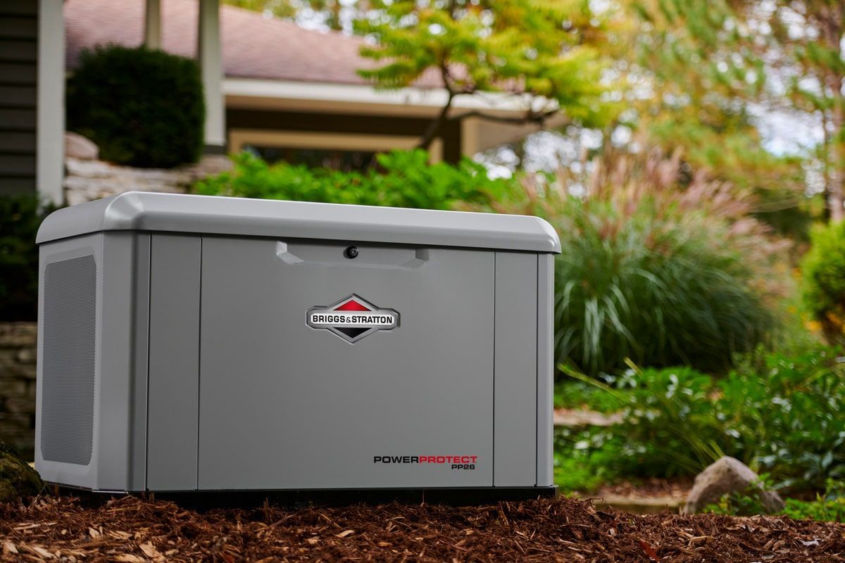 Gray Briggs & Stratton standby generator in a yard with landscaping.