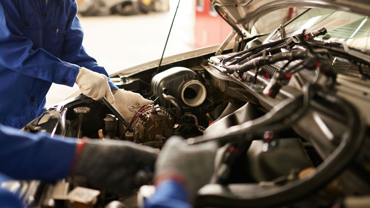 Gloved mechanic working on exposed engine components in a garage under warm light
