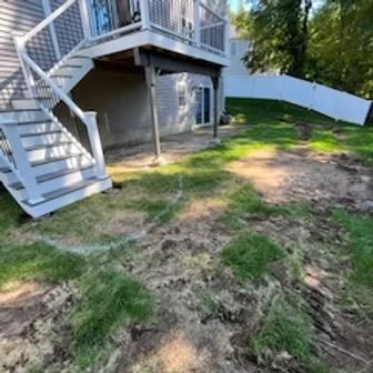 A backyard with a wooden deck, stairs, and patchy grass.