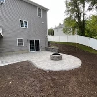 Backyard patio with gray pavers, fire pit, and a two-story house with gray siding.