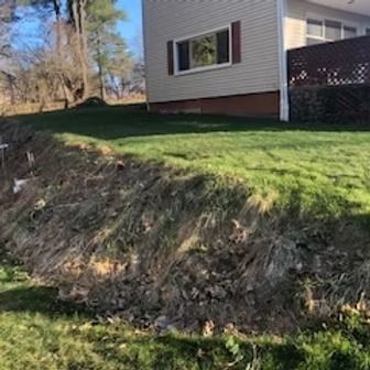 A house with a yard on a sloped hill. Grass in the yard is green.