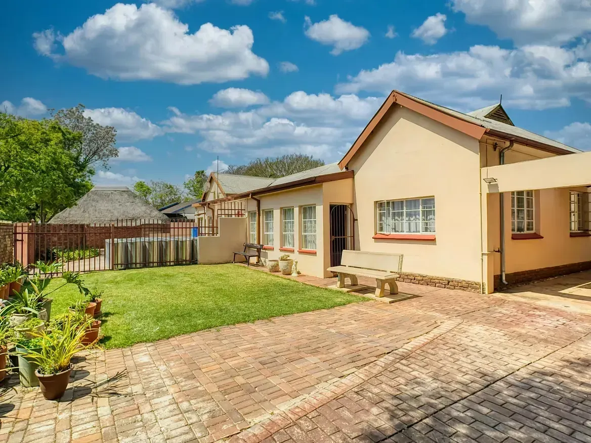 Tan house with brick driveway and green lawn, blue sky with clouds.