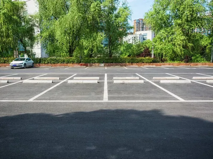 Empty asphalt parking lot with white lines, concrete parking stops, and a parked car.