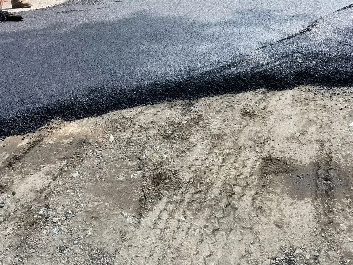 Fresh asphalt pavement meeting a sandy, unpaved surface.