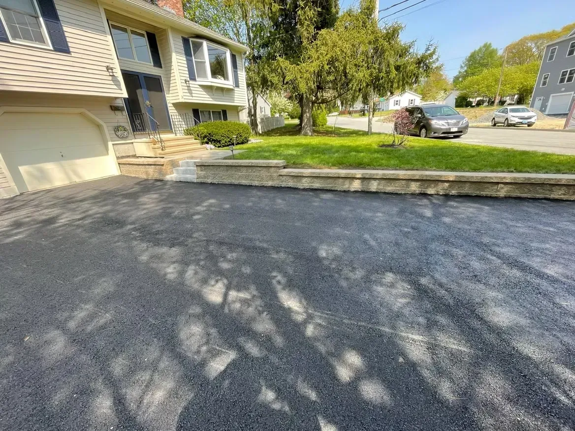 Newly paved driveway in front of a house, with green grass and trees visible.