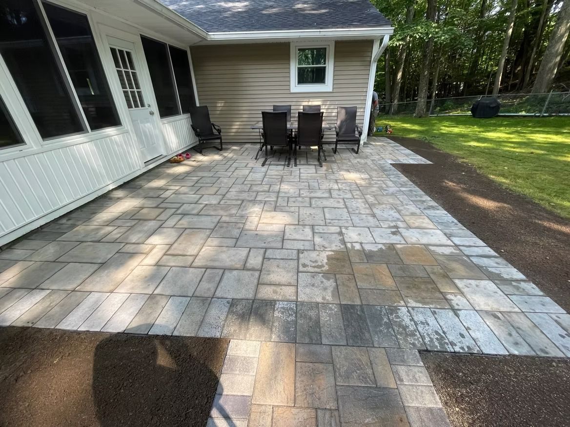 Paver patio with outdoor furniture near a house and grass.
