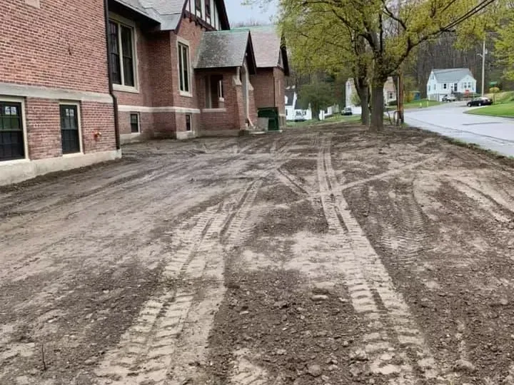 Muddy dirt area with tire tracks in front of a brick building.