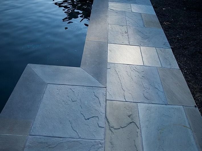 Poolside view, showing light gray stone tiles bordering a dark blue pool.
