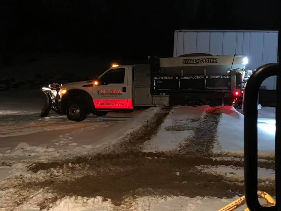 Snow plow truck at night, clearing snow. Orange lights on, red side detail.