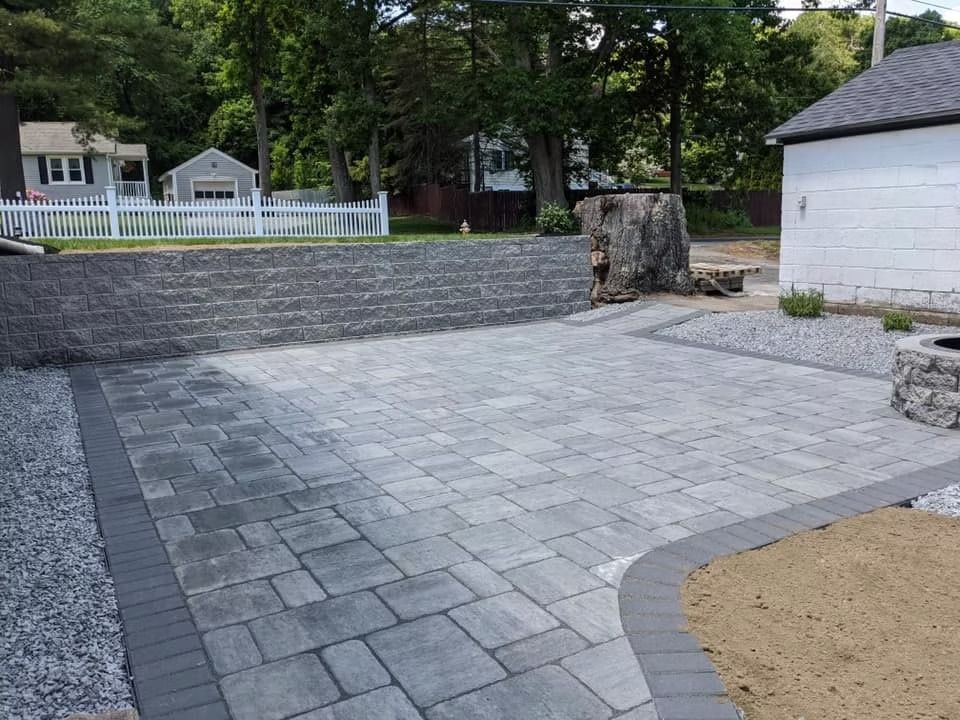 Paver patio with retaining wall, gravel, and large tree stump.