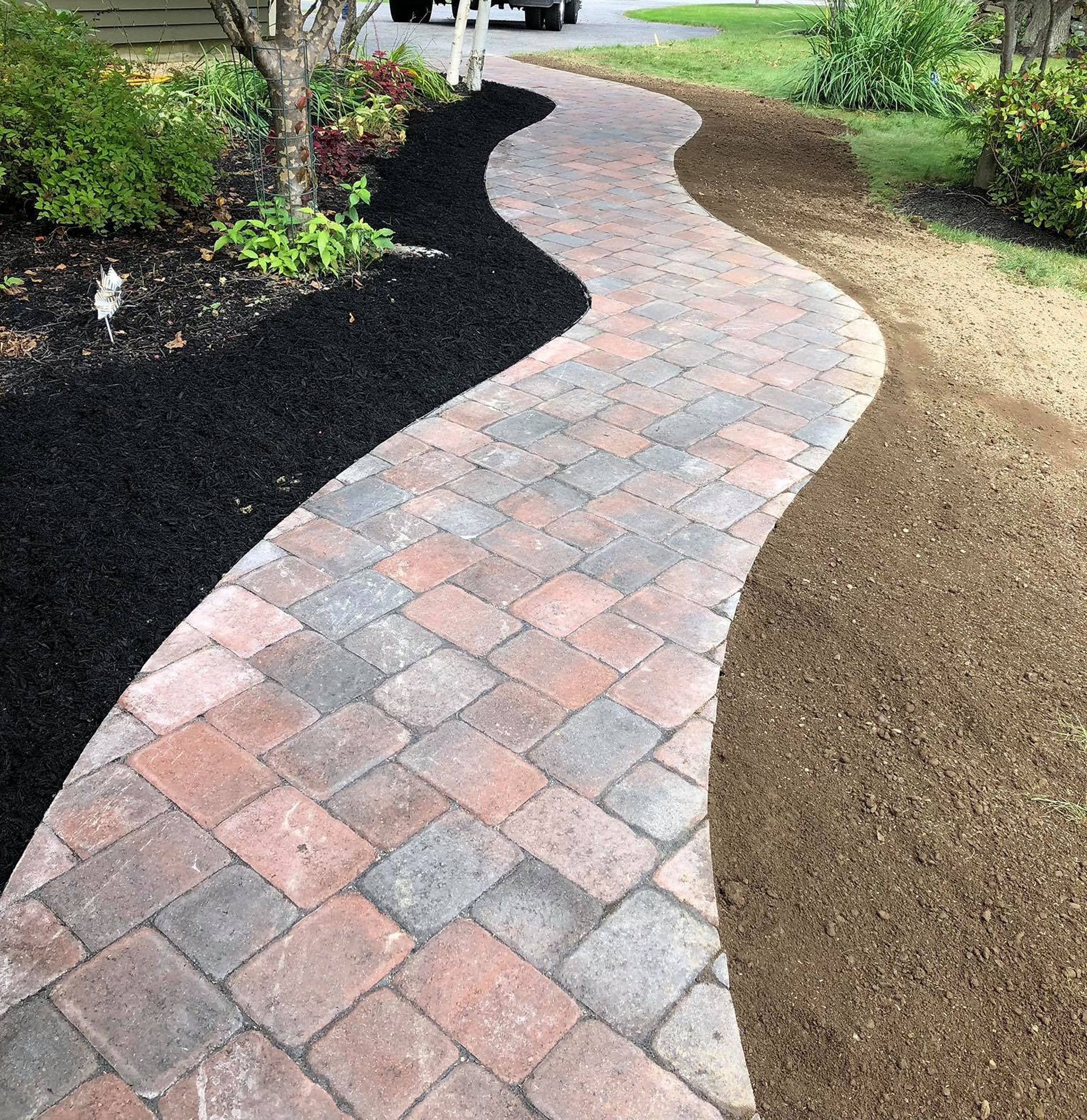 Brick pathway winds through landscaped yard with black mulch and brown gravel.