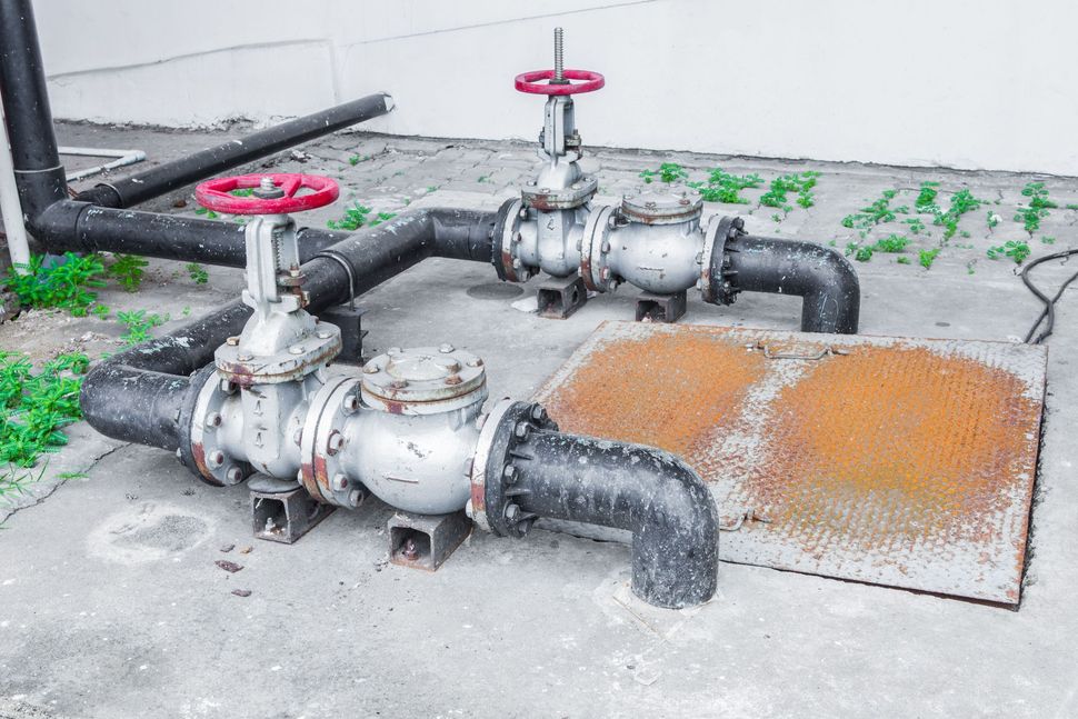 Two industrial metal valves connected to black pipes on a concrete ground surface.