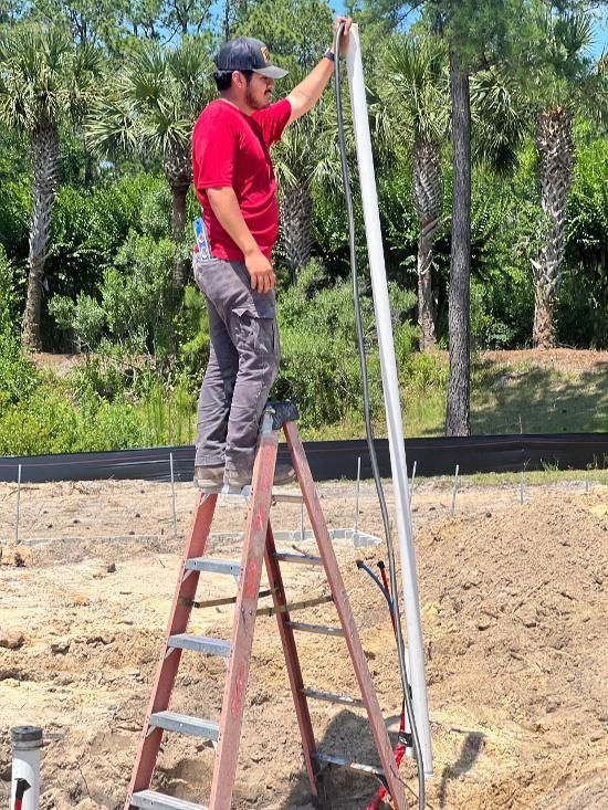 A man is standing on a ladder measuring a pipe.