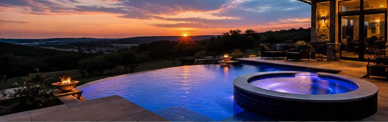 Sunset view of a modern patio with an infinity pool and glowing hot tub overlooking a scenic landscape