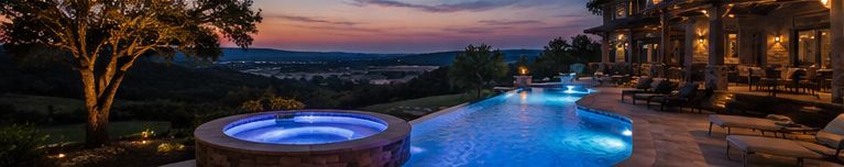 Luxury backyard pool and hot tub at sunset with glowing blue water and a distant ocean view