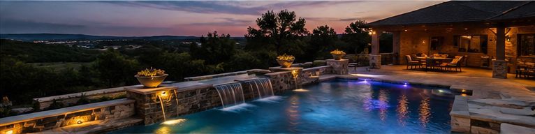 Illuminated backyard pool and waterfall at dusk with blue water and warm patio lights