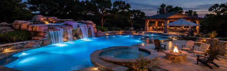 Luxury backyard pool with waterfalls, hot tub, and lit patio at dusk