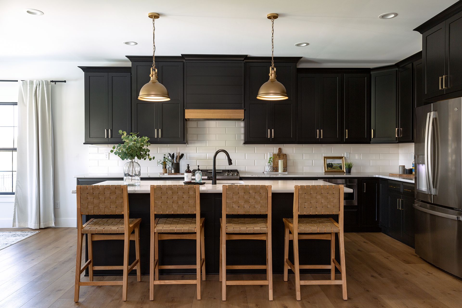 A kitchen with black cabinets , a large island , and wicker bar stools.