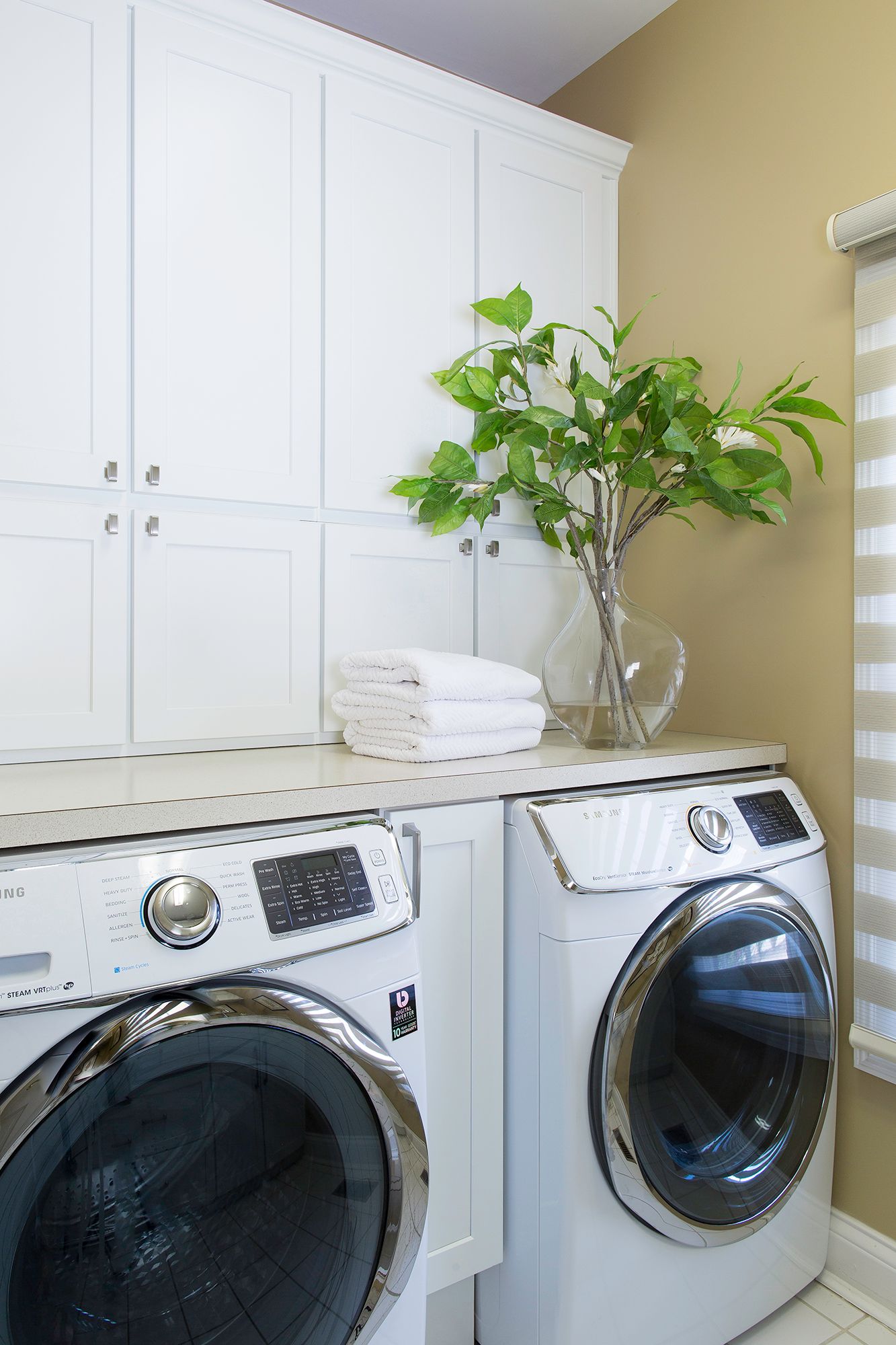 A laundry room with a washer and dryer and a vase of flowers on the counter.