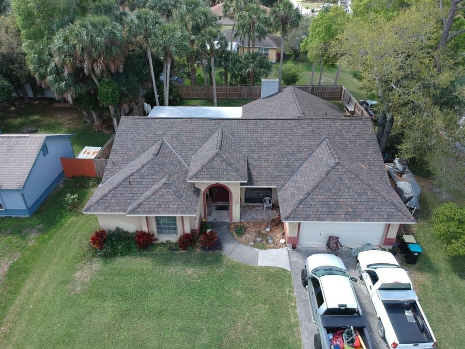 An aerial view of a house with a new roof and trucks parked in front of it.
