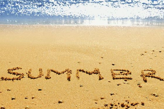 The word summer is written in the sand on a beach.