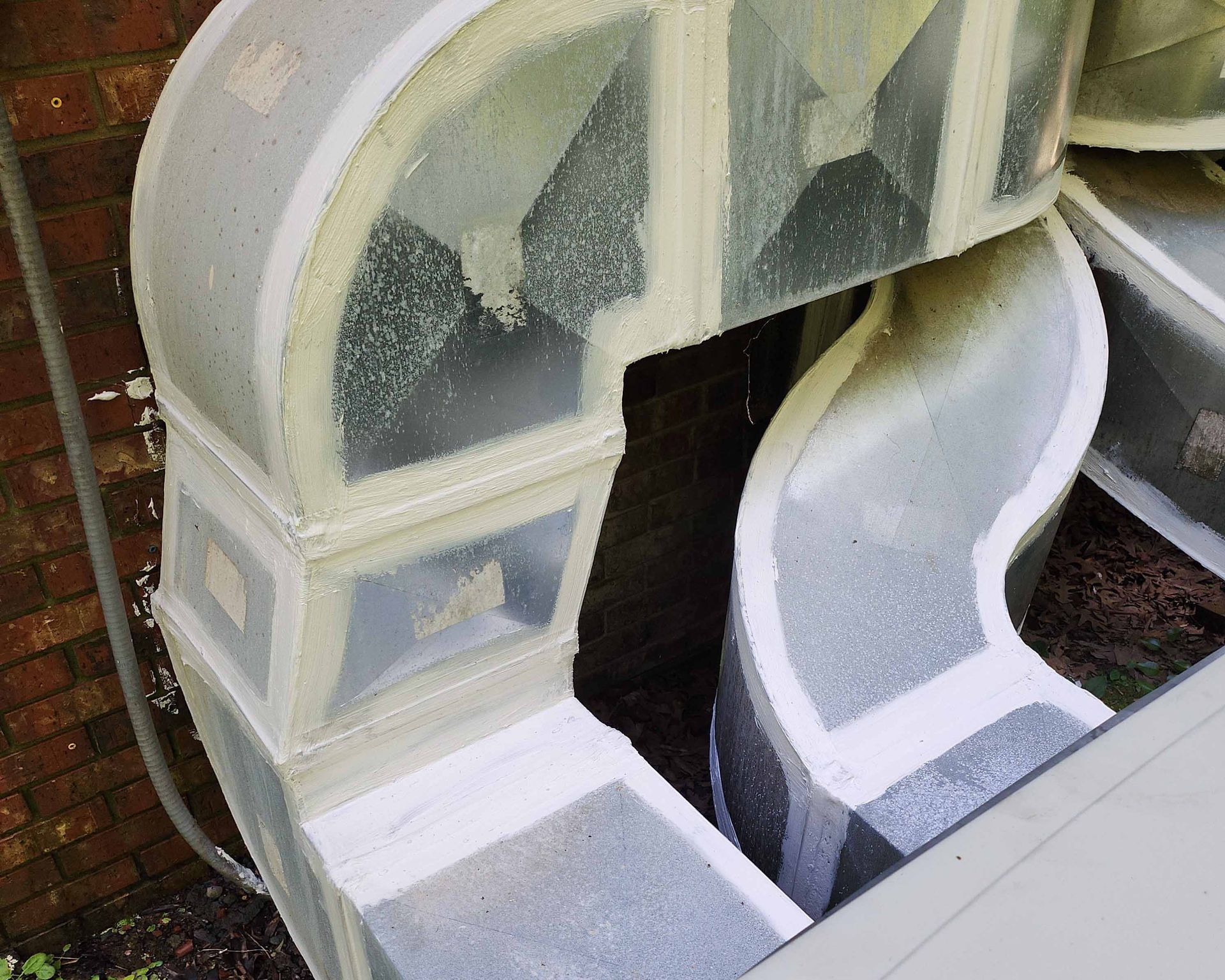 A white duct with a brick wall in the background