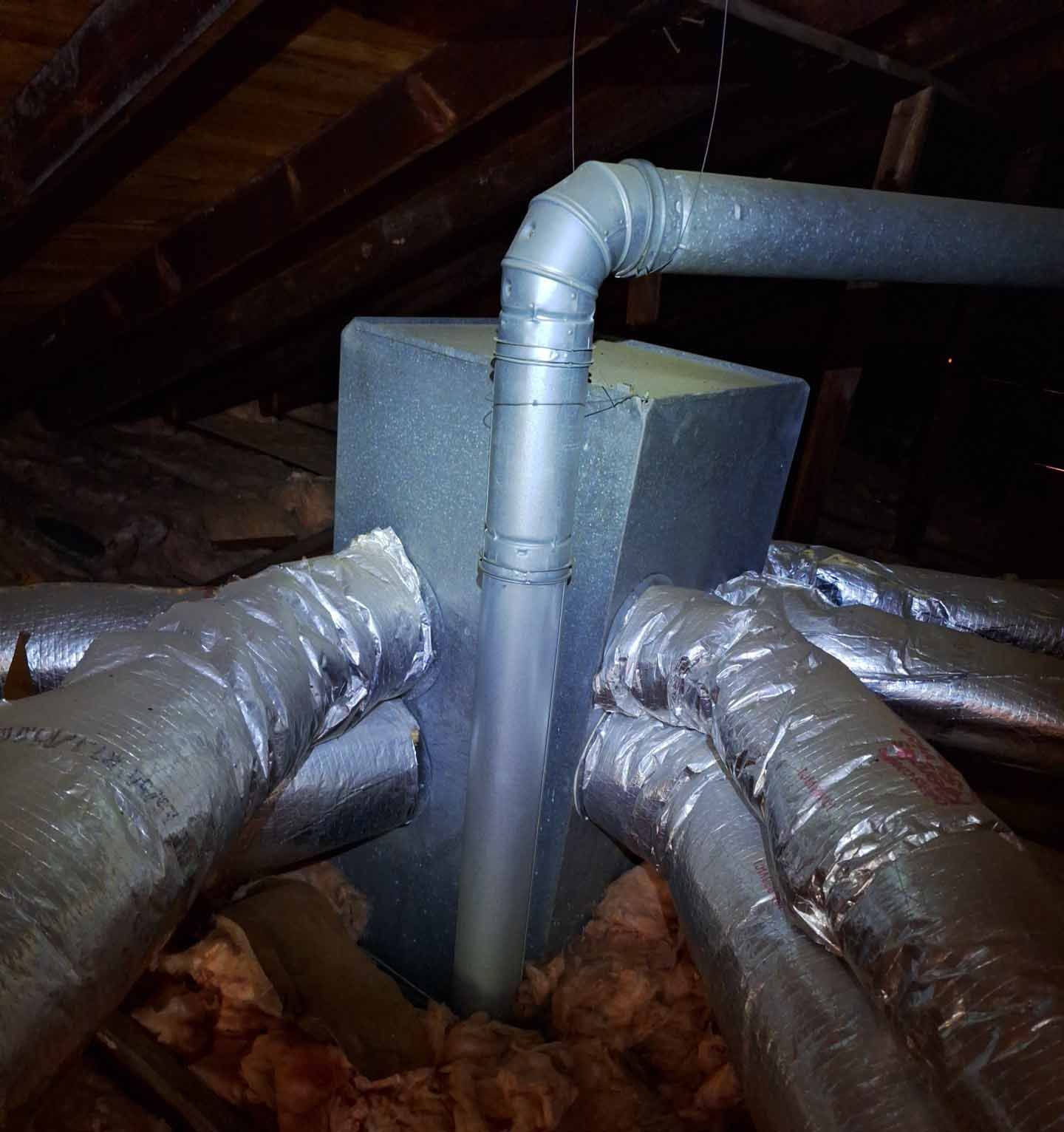 A bunch of pipes are wrapped in foil in an attic
