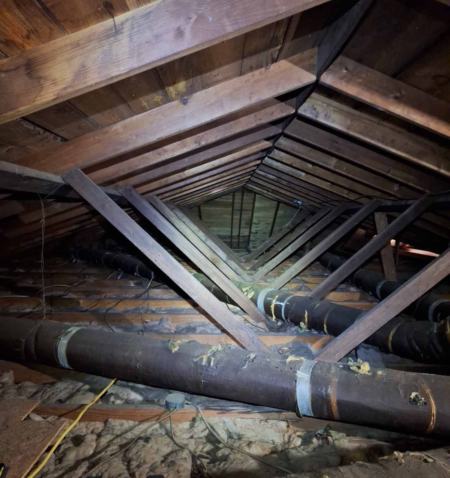 An attic with a lot of pipes and wooden beams