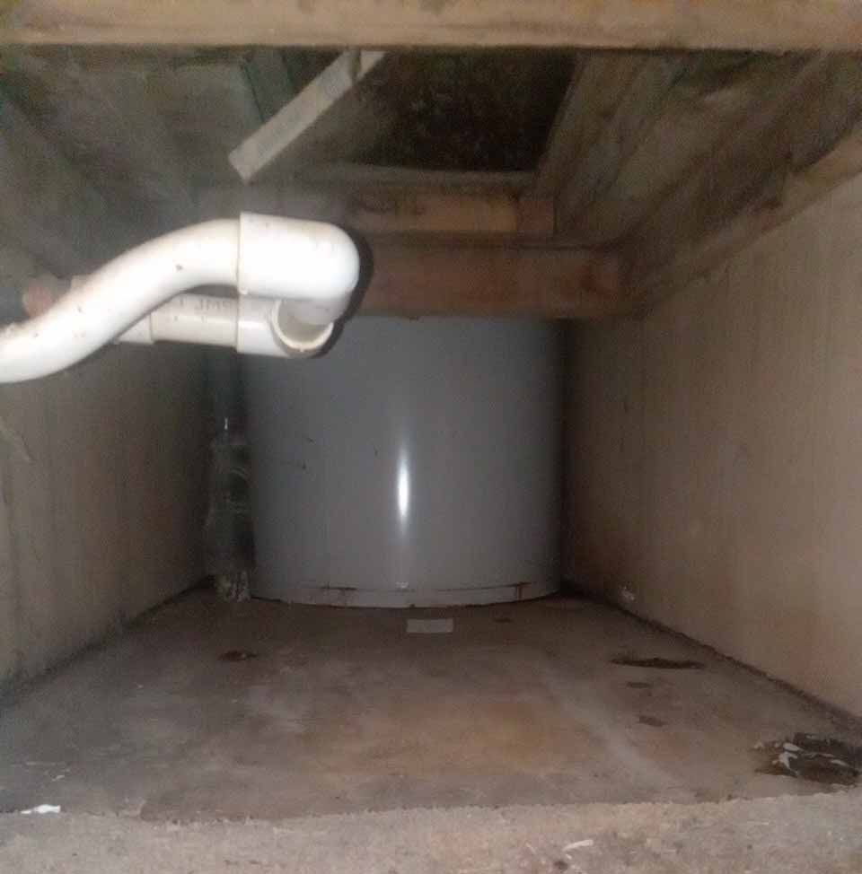 A white water heater is sitting under a wooden ceiling in a basement.
