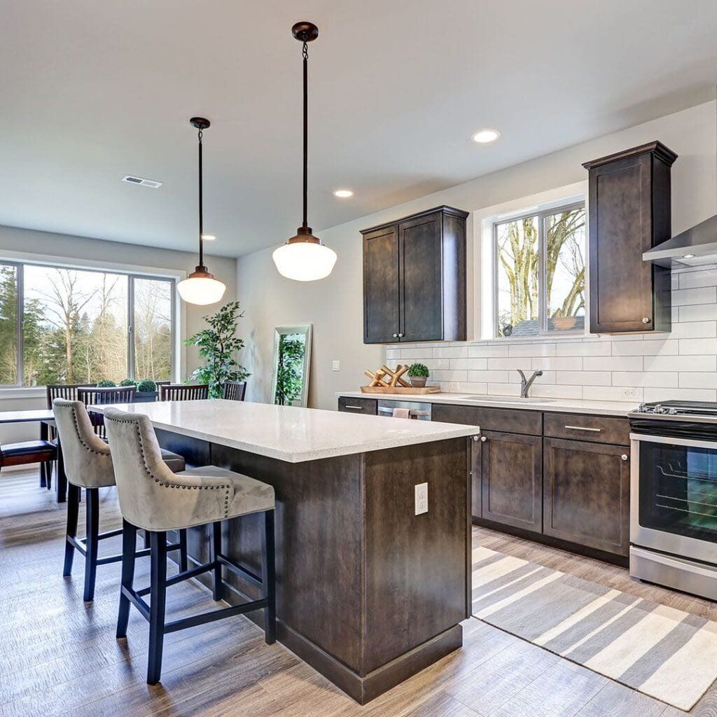 Modern kitchen with island, pendant lights, dark brown cabinets, and a rug.