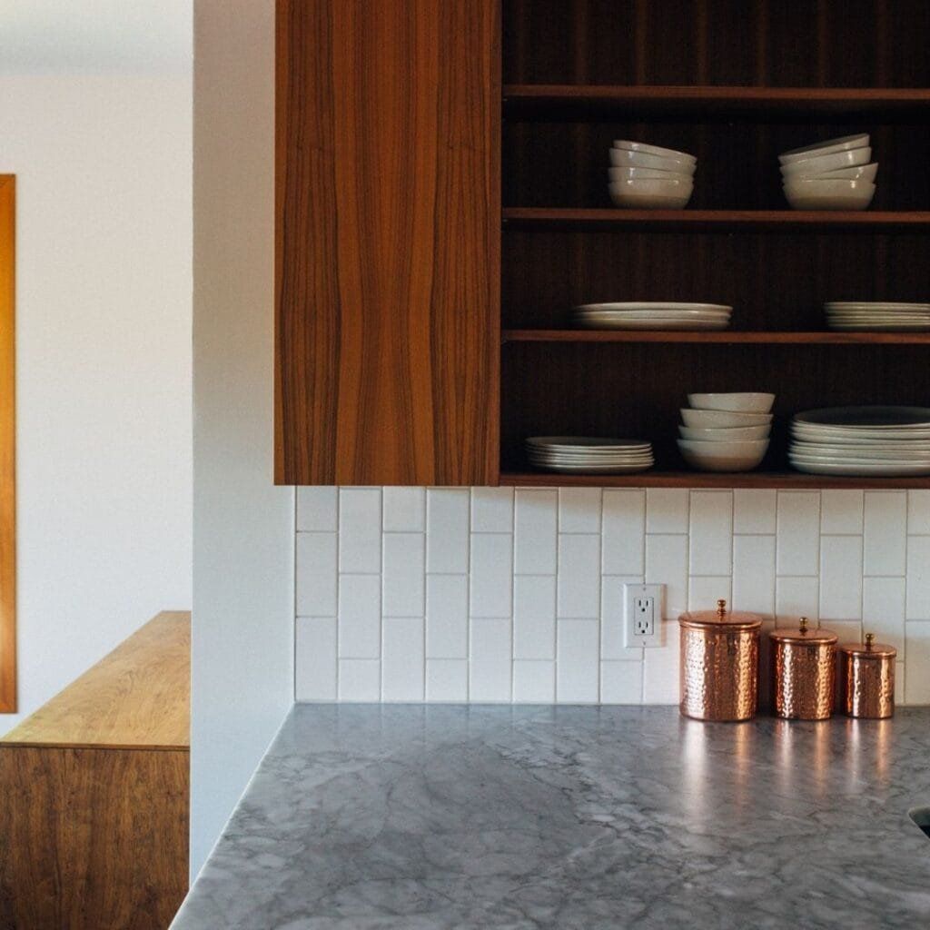 Kitchen counter with marble surface, white tiled backsplash, wood cabinets, and copper canisters.