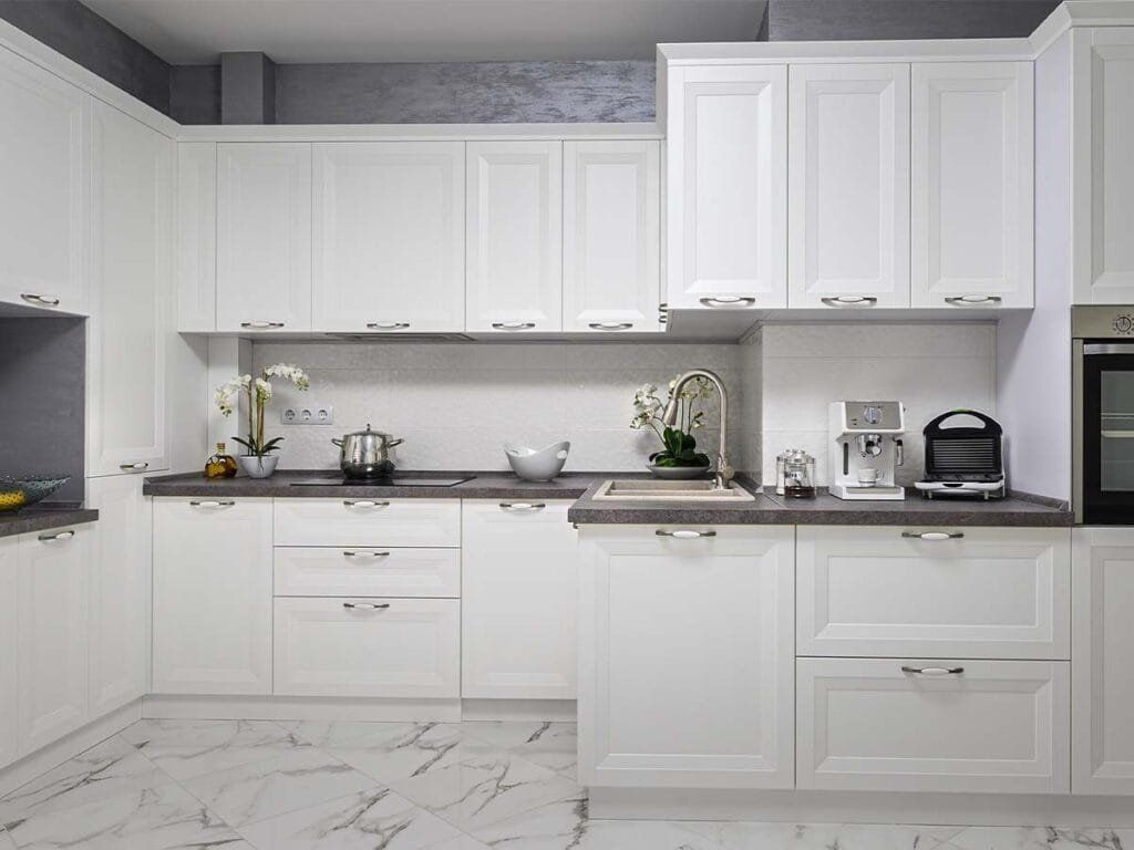 White kitchen cabinets with dark countertops and marble flooring.