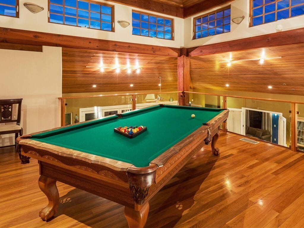 Pool table in a wood-paneled room, balls racked, with natural light from windows above.