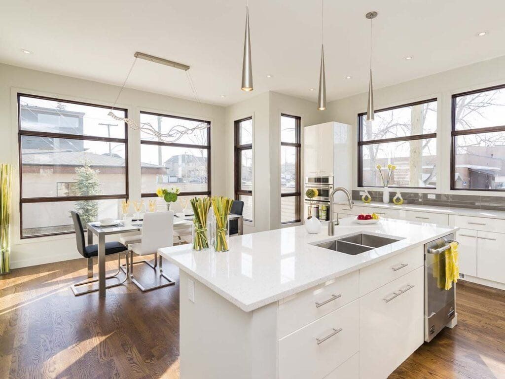 Modern white kitchen with island, stainless steel appliances, and large windows.
