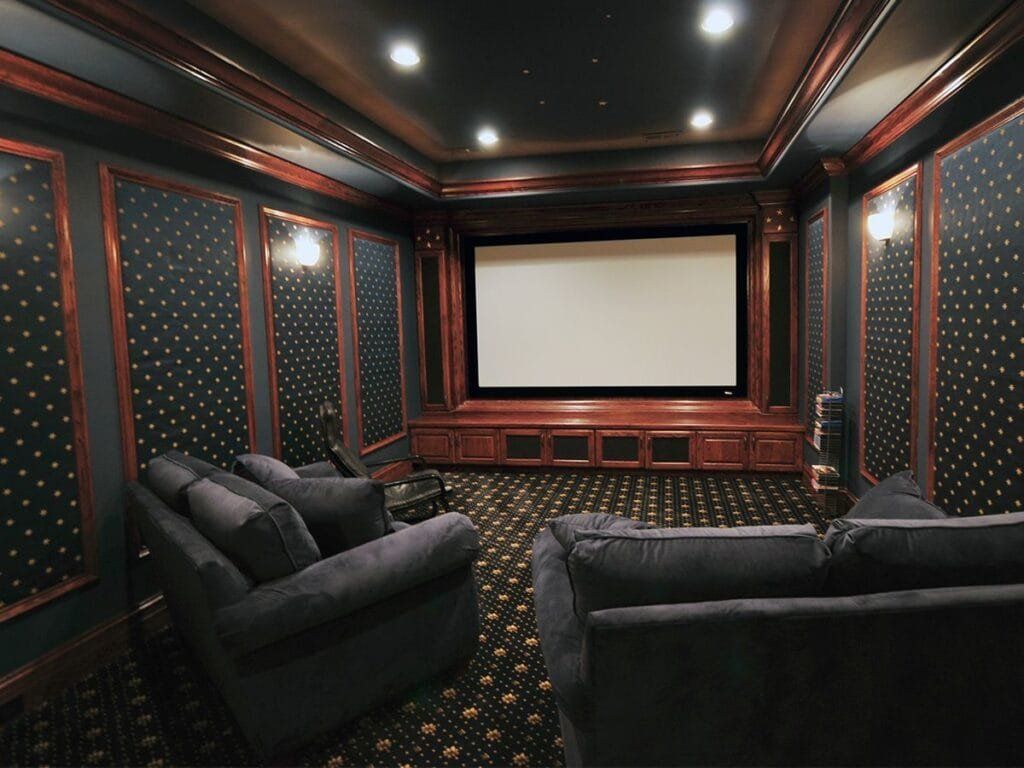 Home theater with dark walls, wooden trim, and a large screen. Two plush couches face the screen.