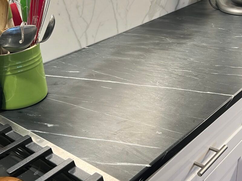 Dark gray countertop with white veining in a kitchen, next to a stove. Green utensil holder on the left.