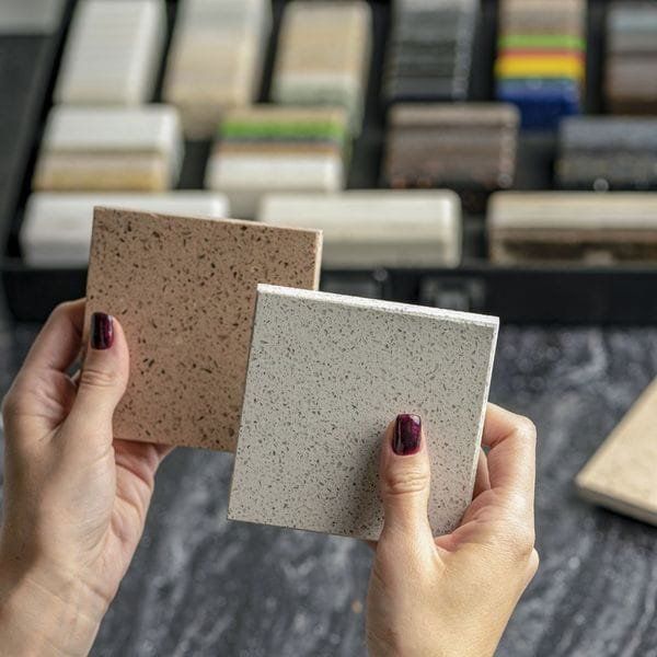 Hands holding brown and white speckled tile samples, other samples in the background.
