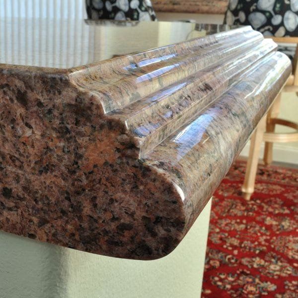 Close-up of a granite countertop edge with a detailed ogee molding. The granite is brown and polished.