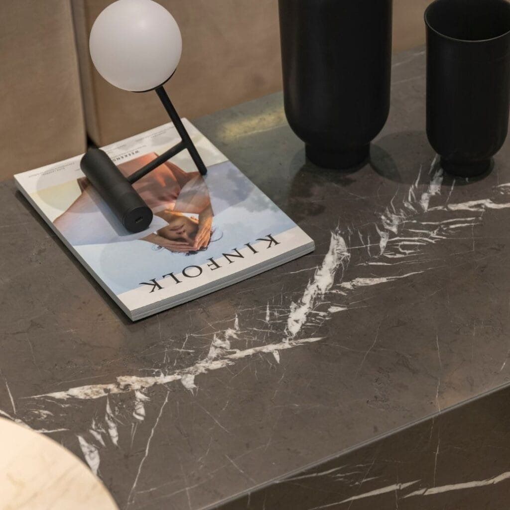 Close-up of a table with a magazine, black lamp, and vases on a gray marbled surface.