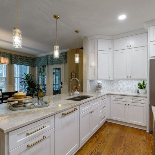 White kitchen with island, cabinets, gold hardware, wood floor, and three pendant lights.