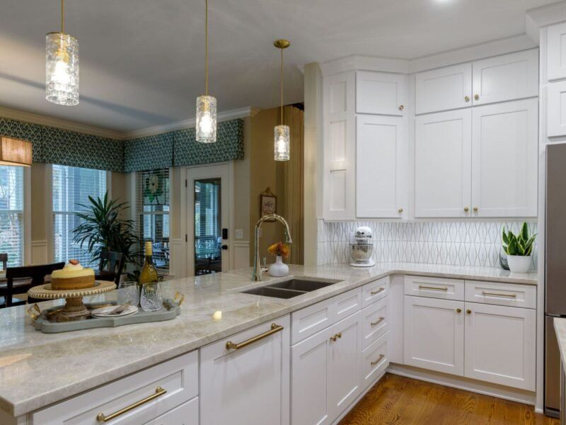 White kitchen with island, cabinets, gold fixtures. Two pendant lights above island, marble countertop, and wood floor.