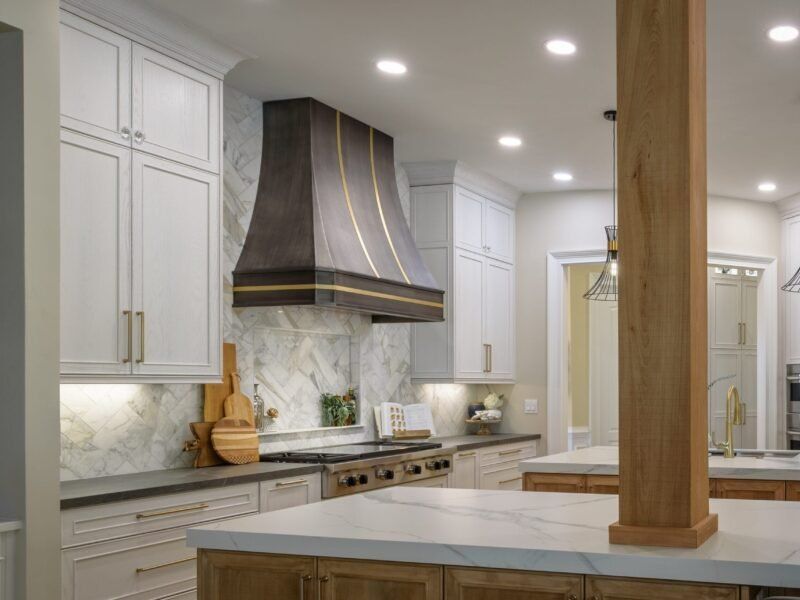 Kitchen with white cabinets, marble backsplash, and a dark range hood with gold trim.