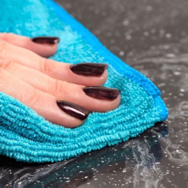 Hand with dark nail polish wiping a blue cloth across a dark, wet surface.