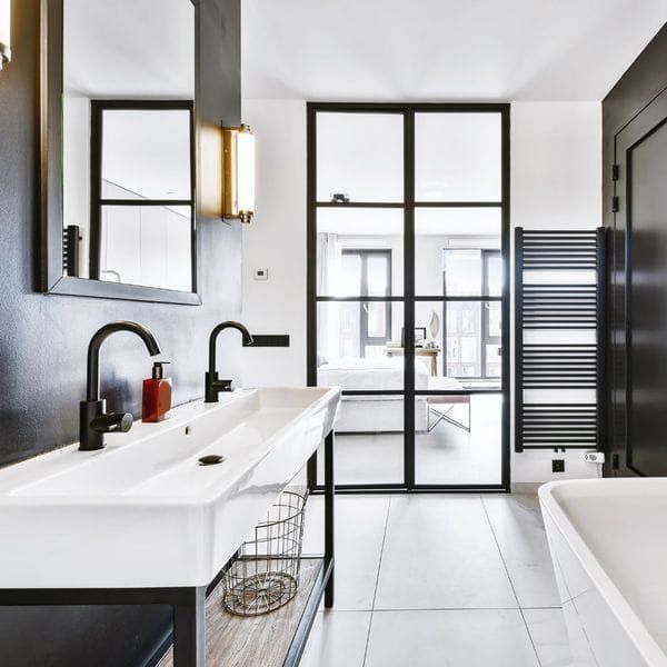 Modern bathroom with black accents, white sink, glass door, and heated towel rack.