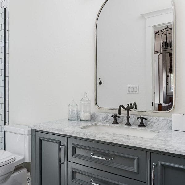 Gray bathroom vanity with marble countertop, black faucet, and arched mirror.
