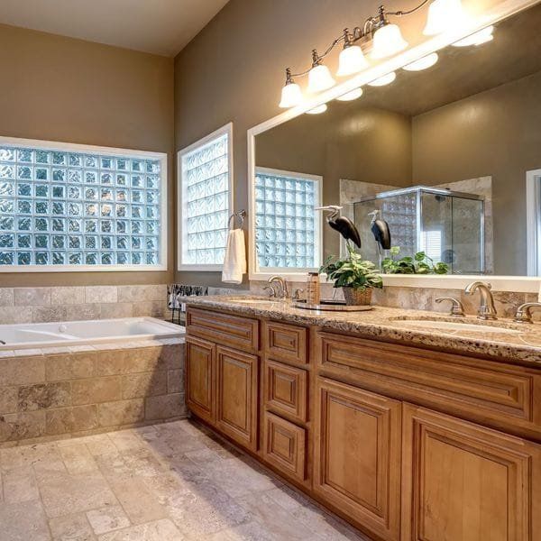 Bathroom with a light brown vanity, marble countertop, large mirror, glass block windows, and a bathtub.