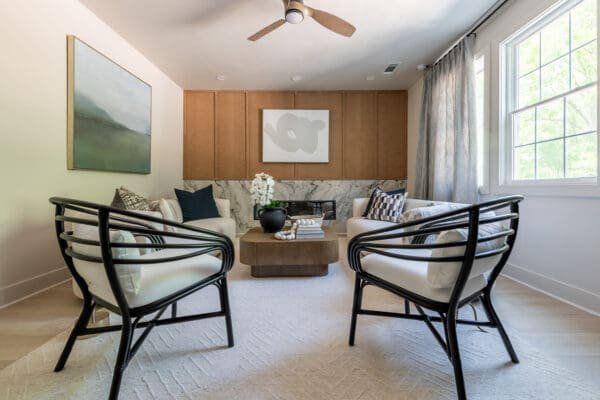 Two black framed chairs face each other in a living room with light-colored walls, a wood panel wall, and a low coffee table.