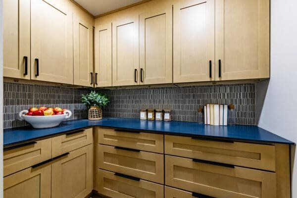 A pantry with light wood cabinets, blue countertops, dark backsplash, and black hardware.
