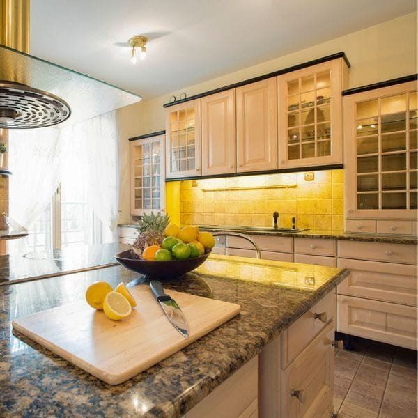 Kitchen with island, granite countertop, fruit bowl, cutting board with lemon, light wood cabinets.